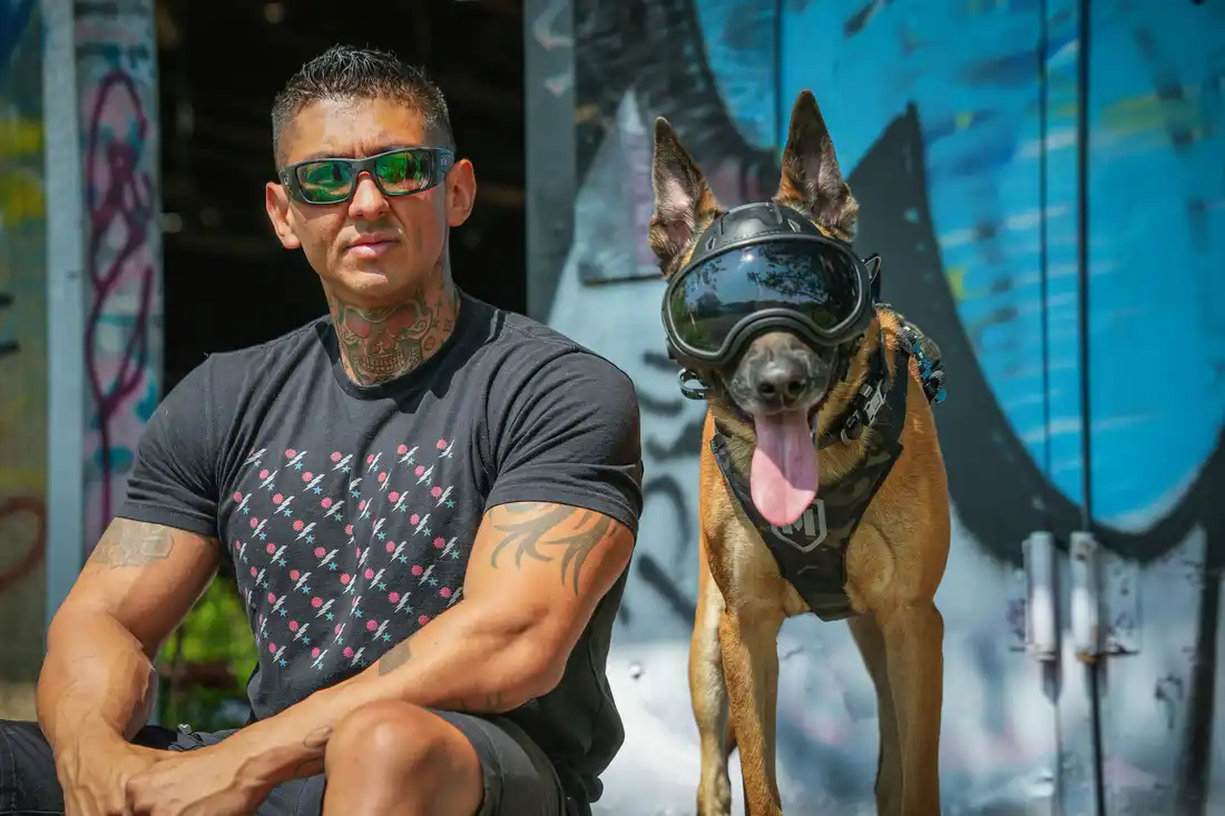 Mike Leal sitting beside a Belgian Malinois wearing protective goggles
